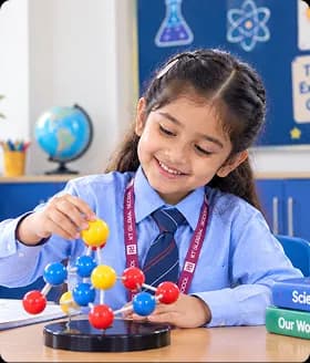 Pre-primary boy student smiling with notebook and pencil at classroom desk